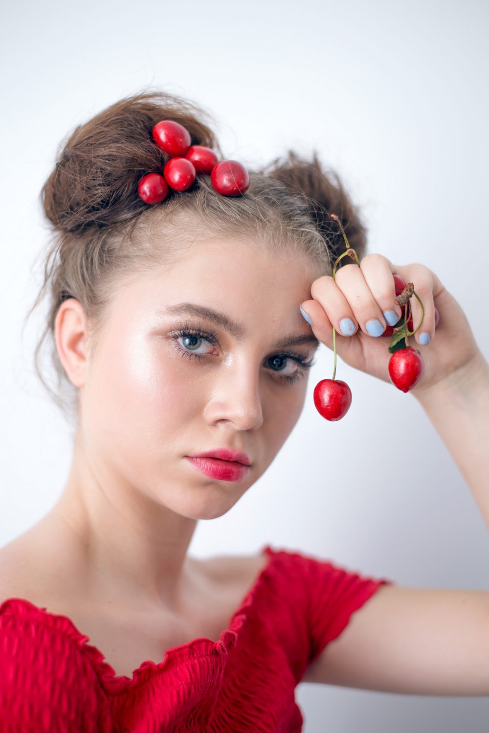 girl with double bun hairstyle holds cherries in one hand