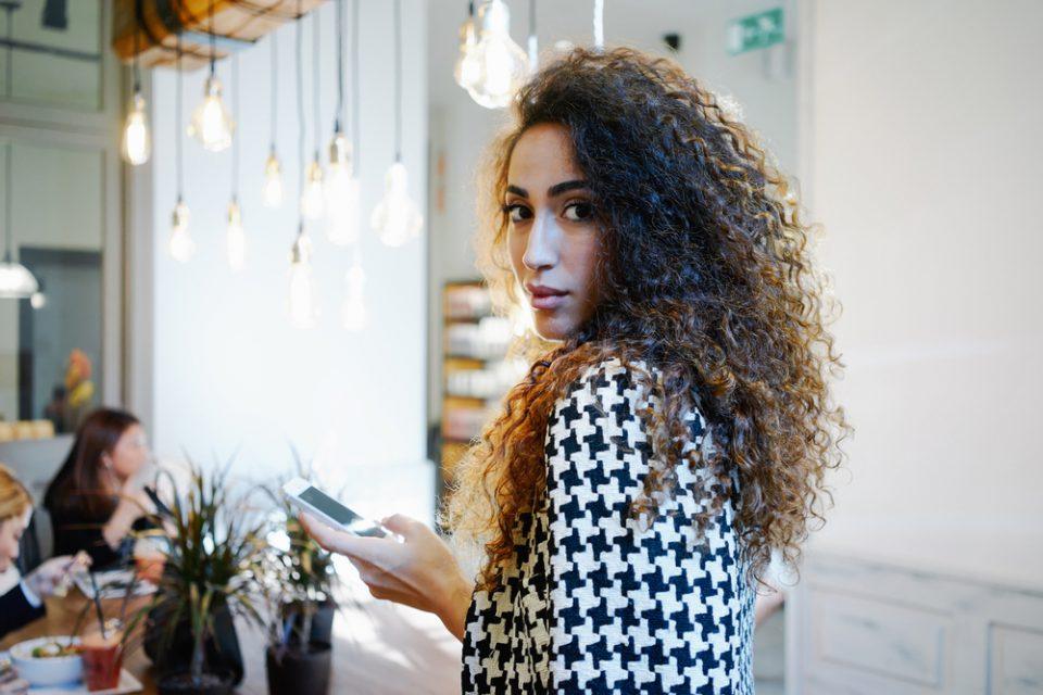 girl looking behind her shoulder with her phone in her hand