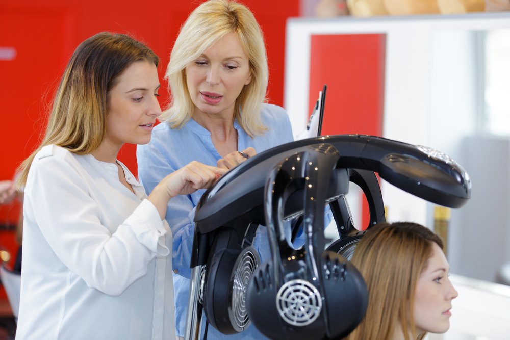 beauty schools student learning how to use a hair dryer with an instructor
