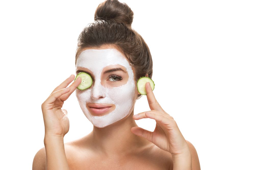 Brunette woman uses a face mask and cucumbers.