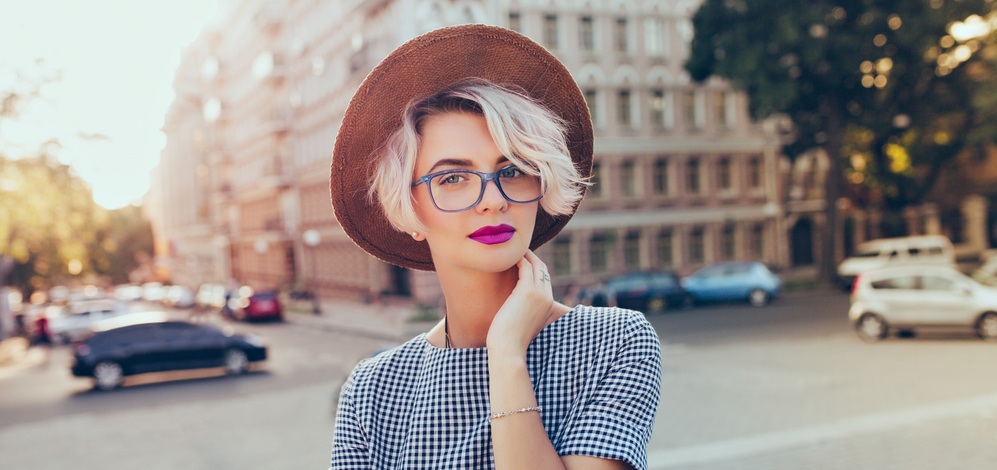 girl with short blonde hair wearing a hat with a city background