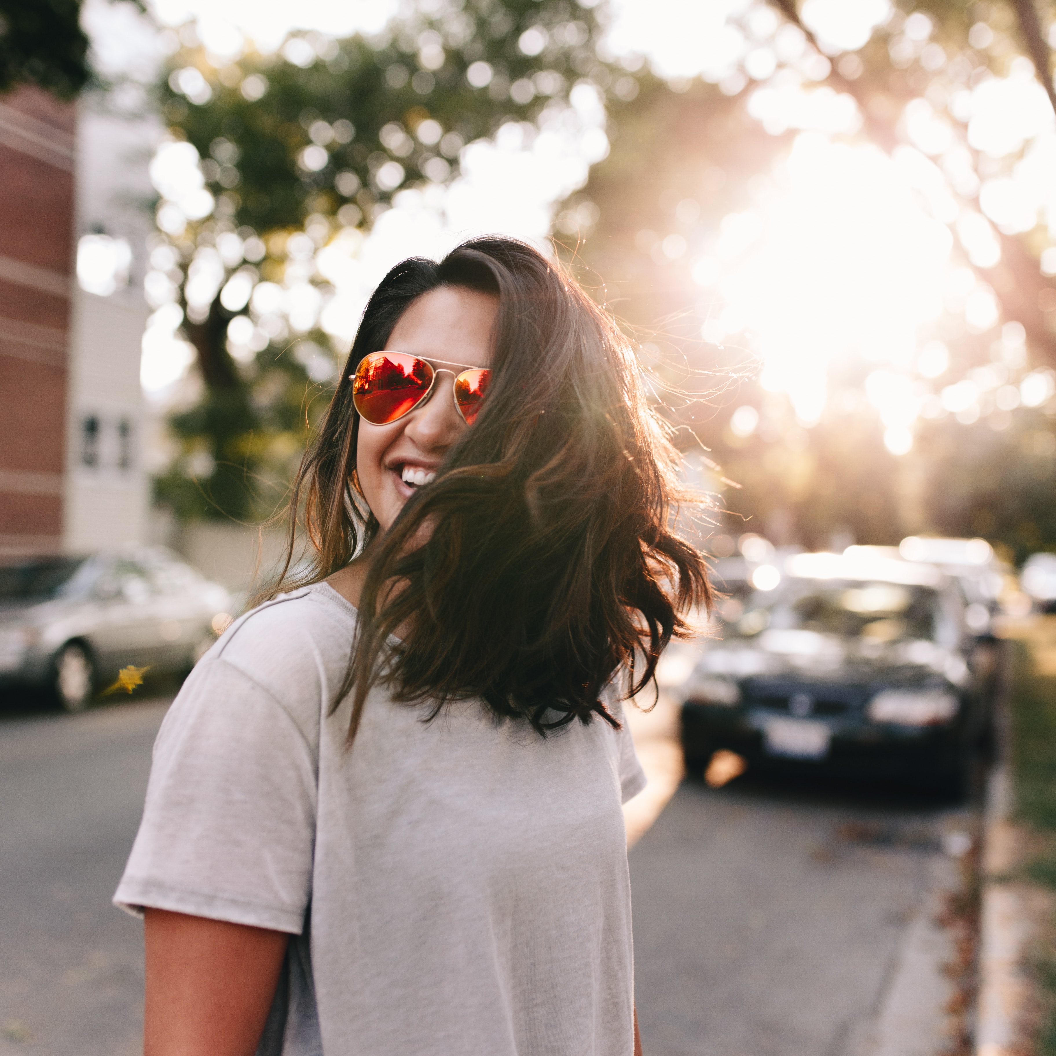 brunette young woman flipping hair in the street with red aviator glasses on 