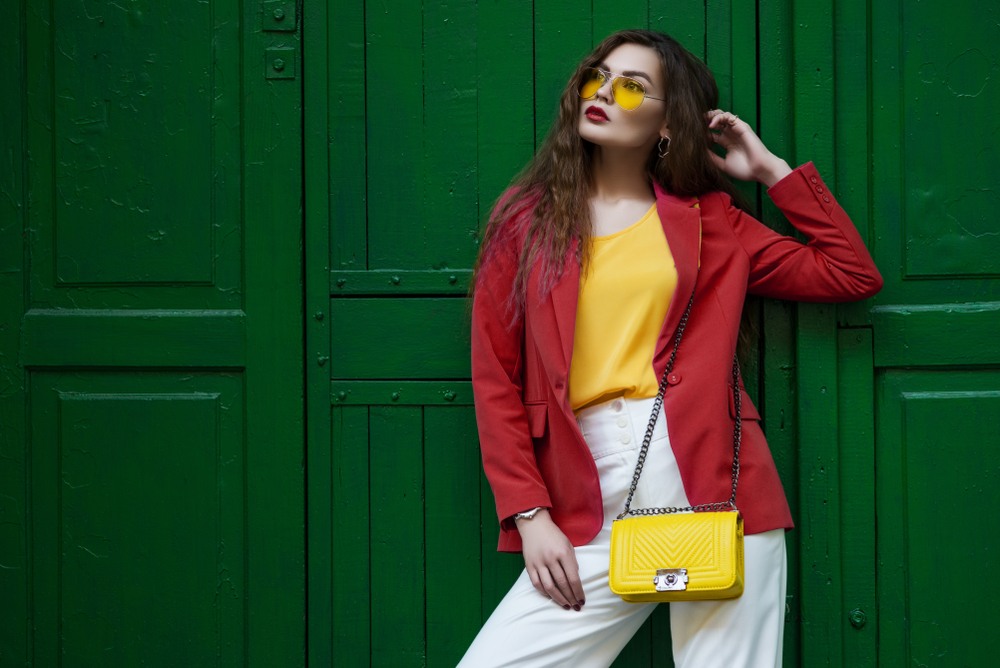 woman wearing yellow glasses standing against green wall