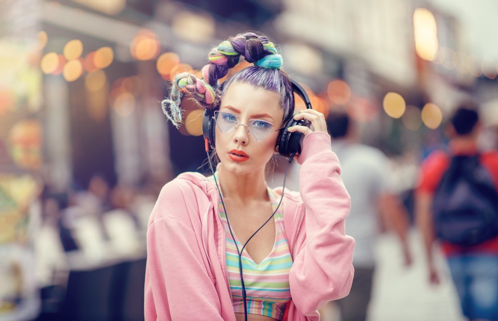 trendy woman with fun colored hair in braided ponytail wearing headphones and triangle glasses