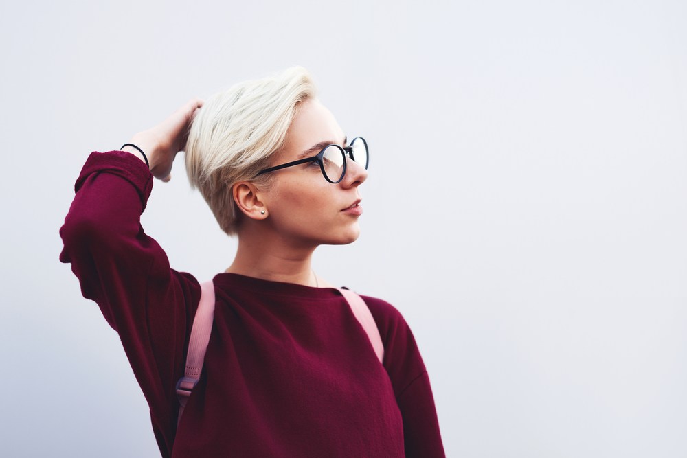 woman with blonde pixie cut and black glasses running fingers through her hair