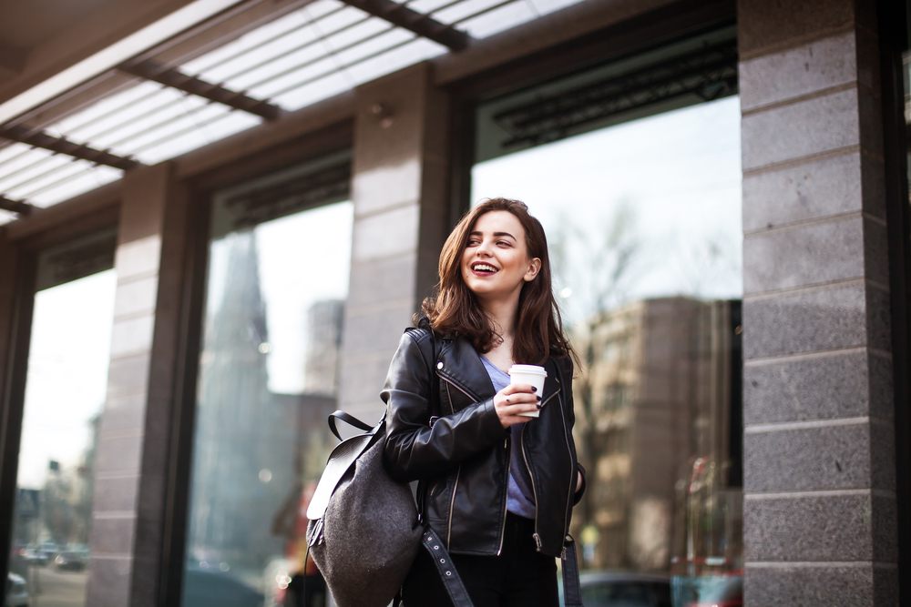 brunette woman in urban area walking with coffee in her hand