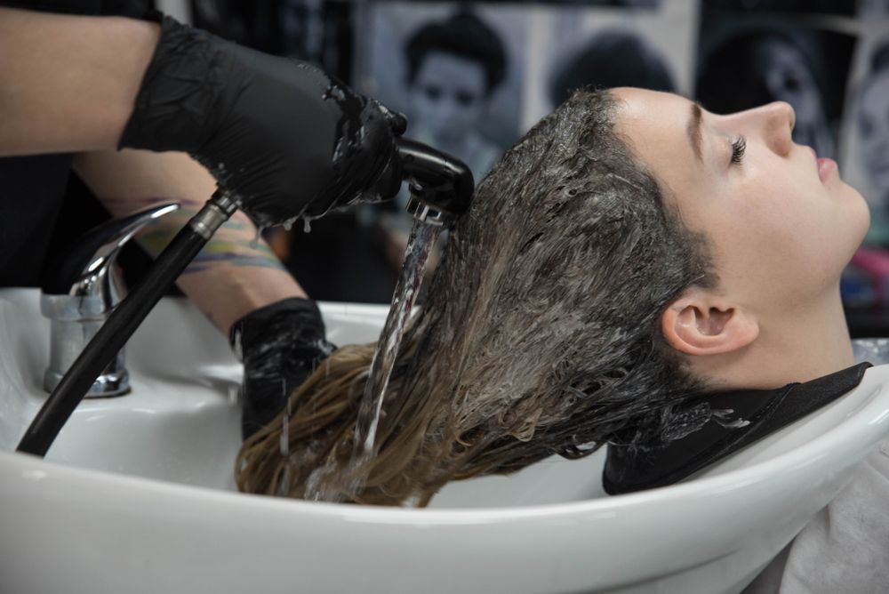 hair stylist washes clients hair over sink