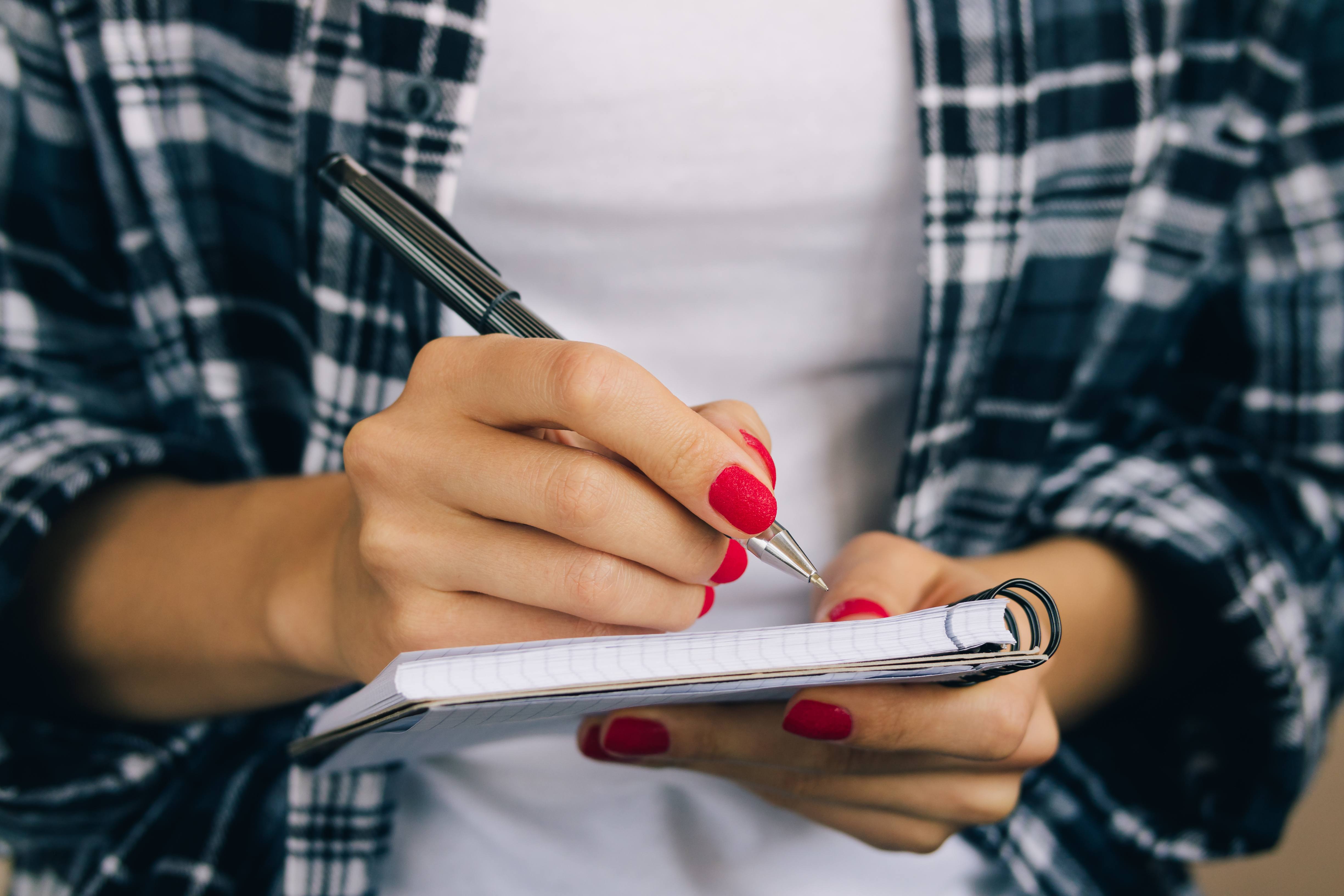 Someone with painted nails writing something in a notebook